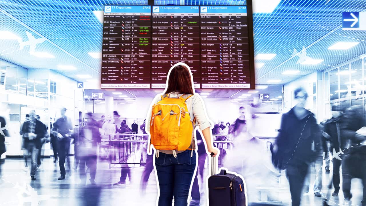 A woman with luggage, looking at an airport departures board.
