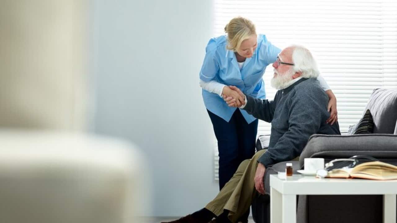 Female caregiver helping senior man get up from couch