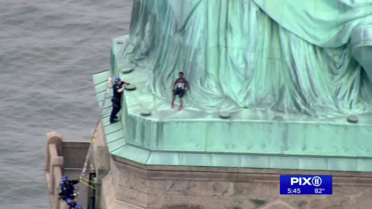 Police officers try to convince the protester to climb down from the pedestal of the Statue of Liberty.