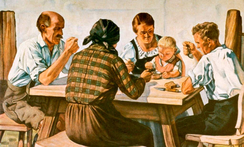 Three generations of an idyllic German country family partake in a family meal in a farmhouse kitchen, circa 1930s.