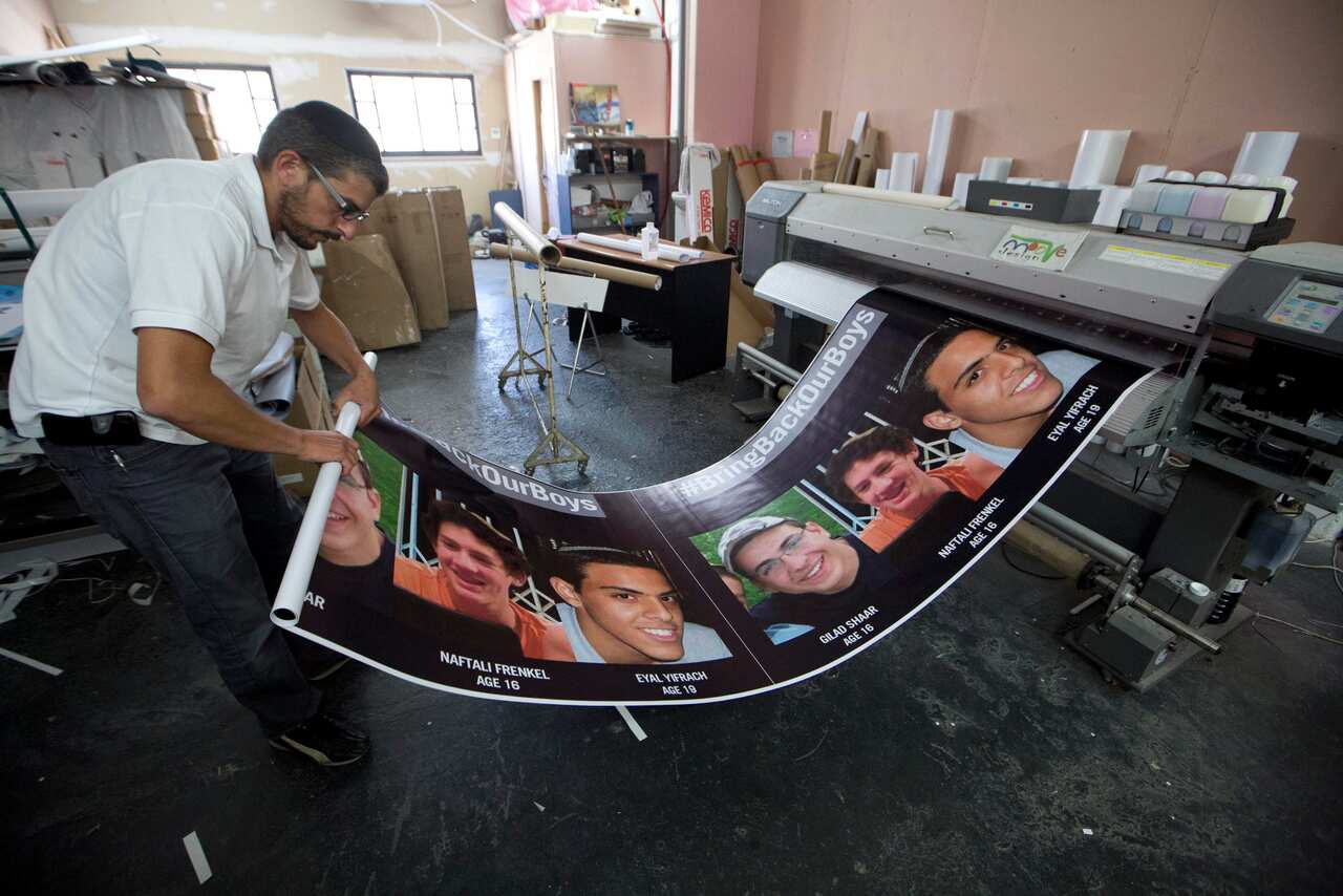 rinting shop owner Jonathan Bracha finishes posters showing Eyal Yifrah, Gilad Shaar and Naftali Frenkel in June. (AAP)