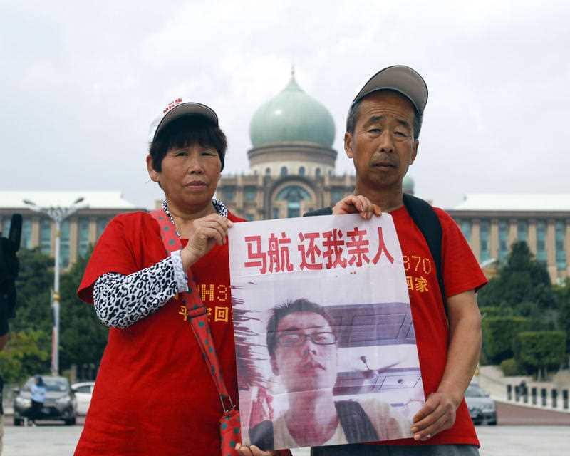 Unidentified Chinese family members of a passenger on board the missing Malaysia Airlines flight MH370 hold up a placard outside the prime minister's office in Putrajaya, Malaysia on Wednesday, Feb. 18, 2015. (AP Photo/Joshua Paul)