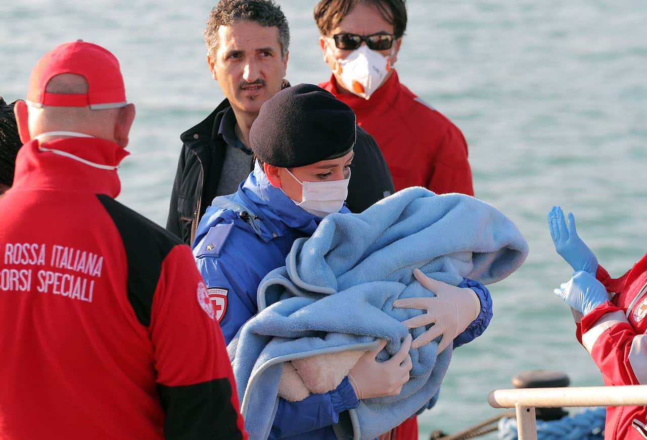 A Red Cross officer carries a baby wrapped in a blanket after surviving migrants disembarked at the Sicilian Porto Empedocle harbor, Italy, (AP Photo/Calogero Montanalampo) 