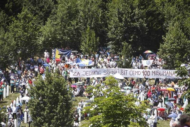 Bosnian Muslim people display a banner reading "For every killed Serb, we will killed 100 Bosniaks (Muslims)" during a visit by Serbian Prime Minister Aleksandar Vucic to the memorial complex of Potocari,