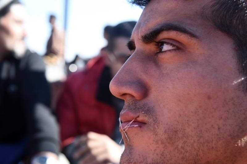 A migrant sits in no-man's land with his mouth sewn shut during a protest near the village of Idomeni at the Greek-Macedonian border, on Monday, Nov. 23, 2015.