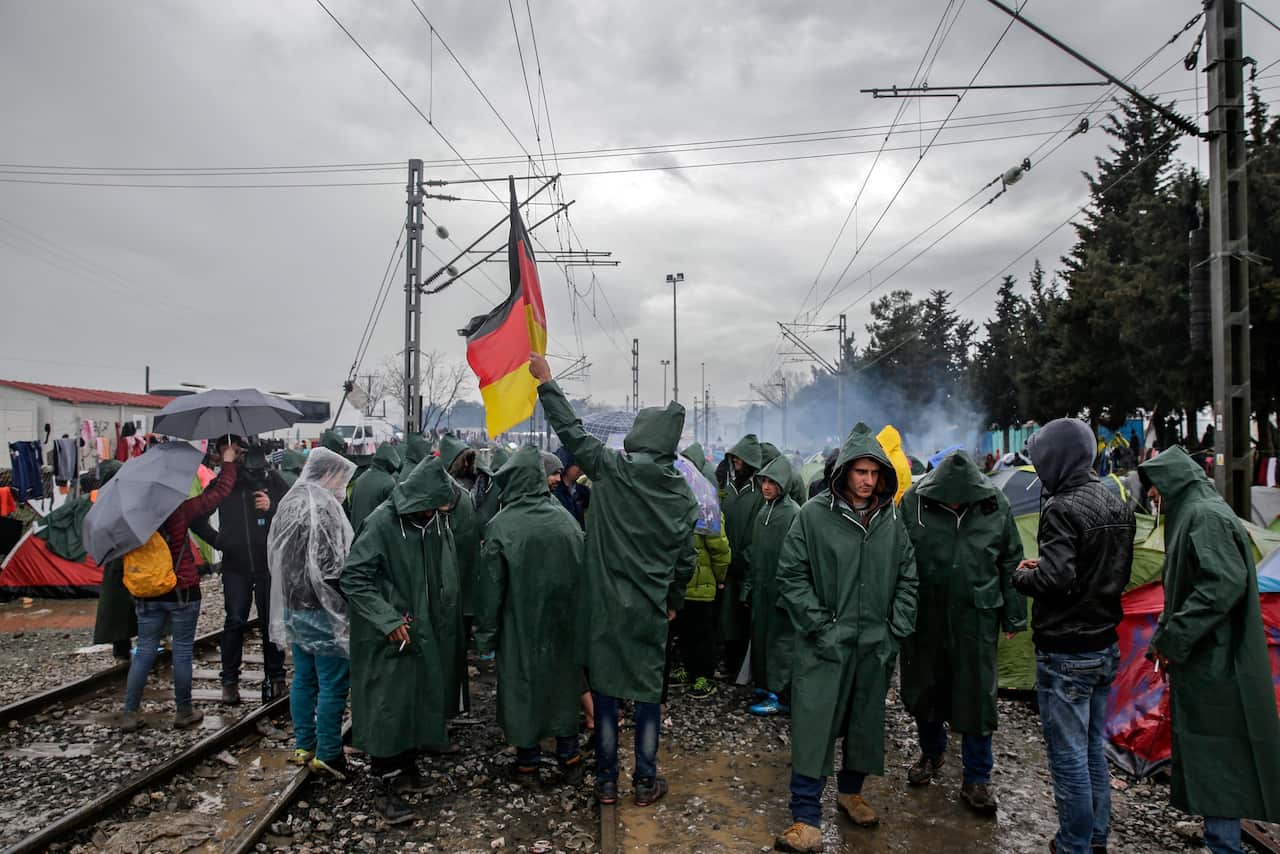 Refugees protest waving a German flag in a refugee camp at the border between Greece and the Former Yugoslav Republic of Macedonia