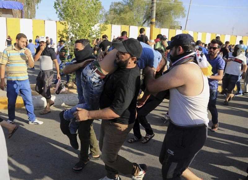 An injured protester is rushed to treatment as Iraqi security forces stand guard outside Baghdad's highly fortified Green Zone