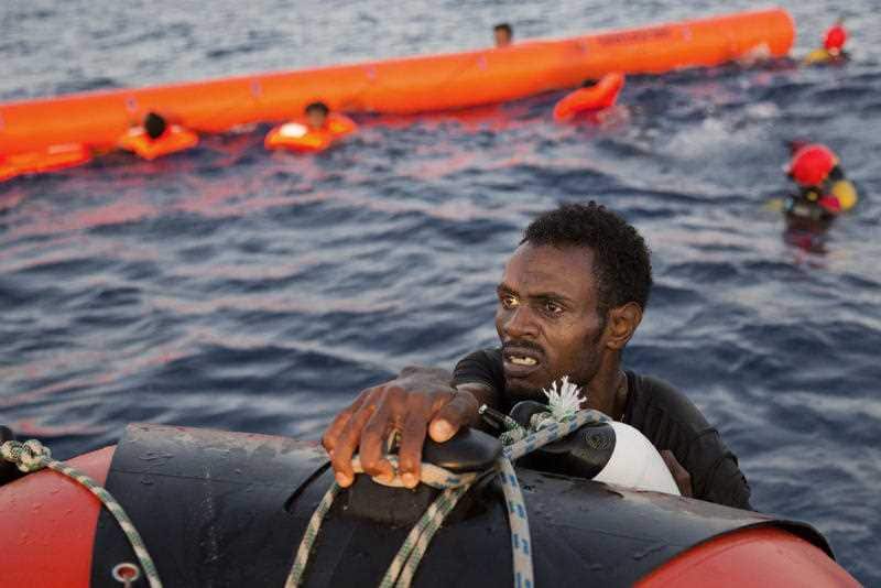 A migrant from Eritrea grabs a RIB after jumping into the water from a crowded wooden boat during a rescue operation at the Mediterranean sea