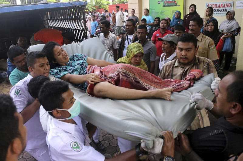 Hospital workers and family members carry a woman injured in an earthquake at a hospital in Pidie, Aceh province, Indonesia