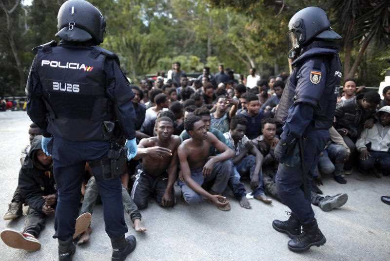 Migrants sit on the ground next to Spanish police officers after storming a fence to enter the Spanish enclave of Ceuta, Spain