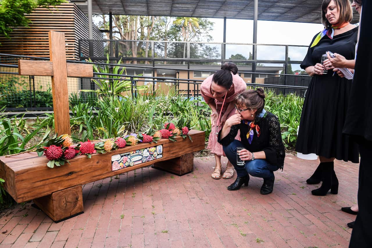 Parents of school children view inscriptions on a memorial bench during a memorial service for the Manrique-Lutz family at St Lucy's School in Wahroonga.