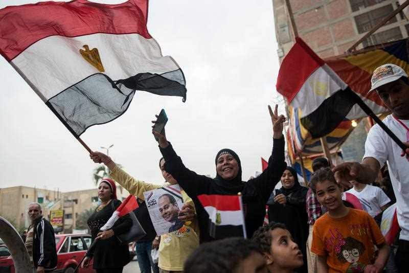 People hold a photo of President Abdel Fattah al-Sisi, and wave national flags on the final day of the Egyptian presidential election 