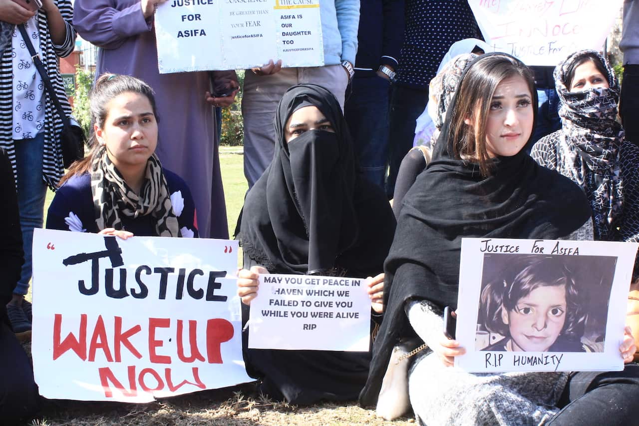 Protesters hold signs as they rally at Pratap Park in Srinagar on April 14, 2018