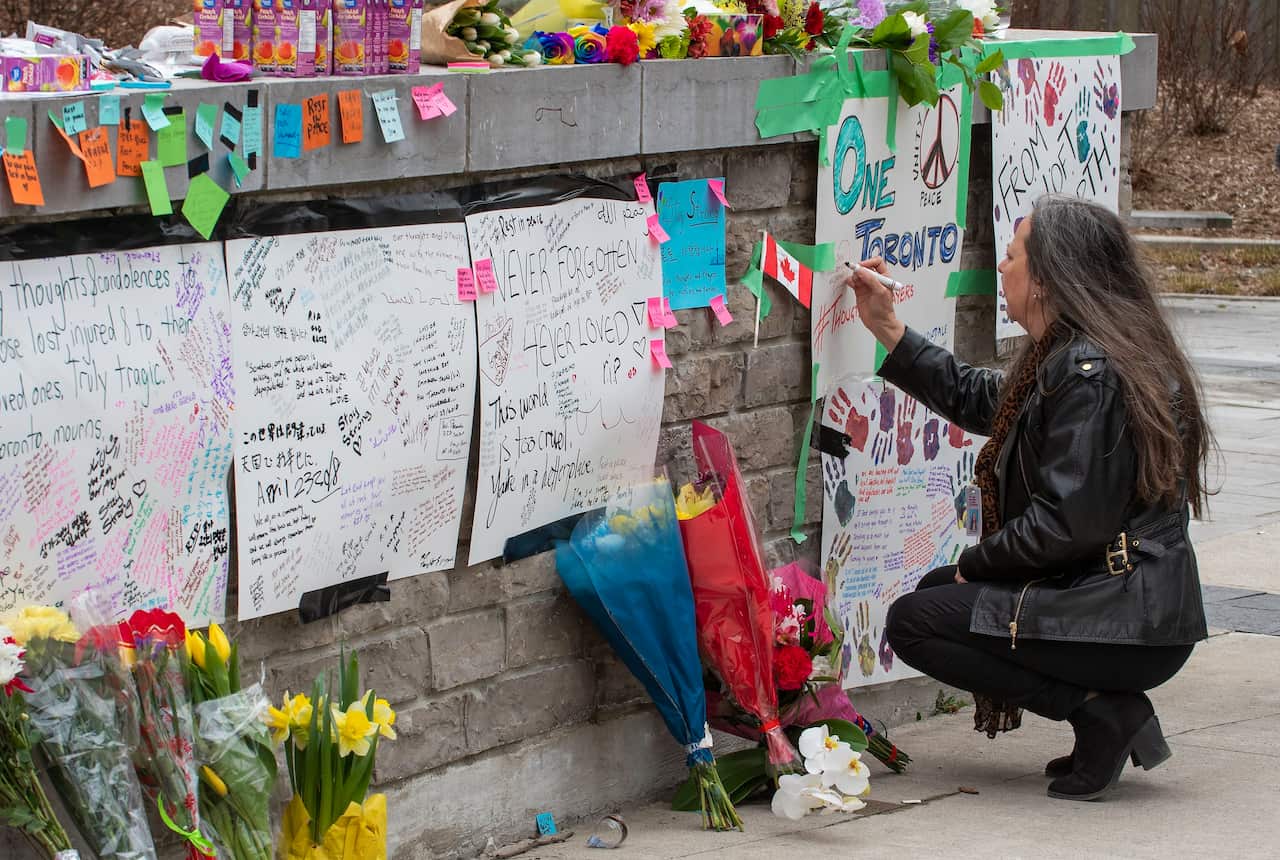 A woman writes a message at a makeshift memorial across the street from where a man in a rented van plowed into pedestrians in Toronto, Canada.