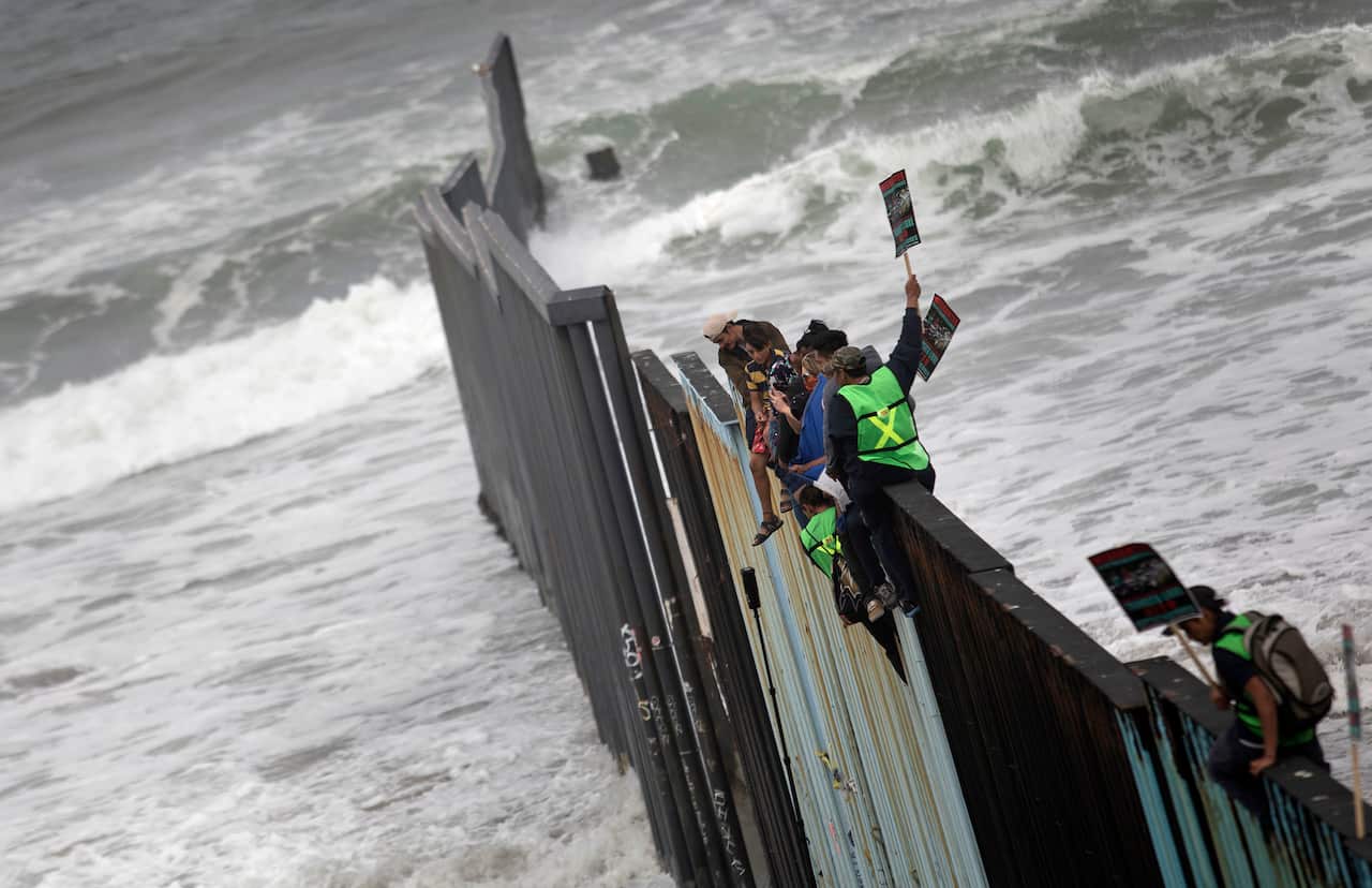 Central American migrants traveling with a caravan sit momentarily on top of the border wall during a gathering of migrants living on both sides of the border.