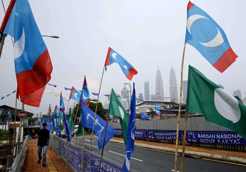 A man walks beside flags from different political parties with the Petronas Twin Towers in the background in Kuala Lumpur, Malaysia, Monday May 7, 2018.