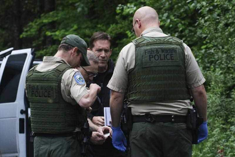Washington State Fish and Wildlife Police confer with an individual from the King County Medical Examiner's and a King County Sheriff's deputy on a remote gravel road above Snoqualmie, following a cougar attack.