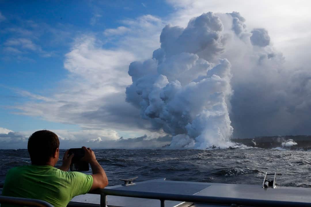 Tourists take pictures as lava enters the ocean.