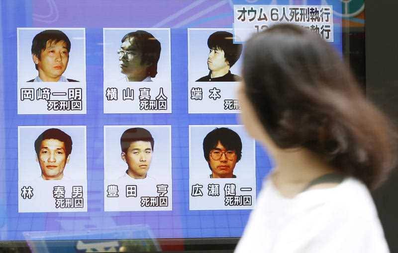 A woman walks on a street while watching TV news reporting executions of six members of Aum Shinrikyo, in Tokyo Thursday, July 26, 2018.