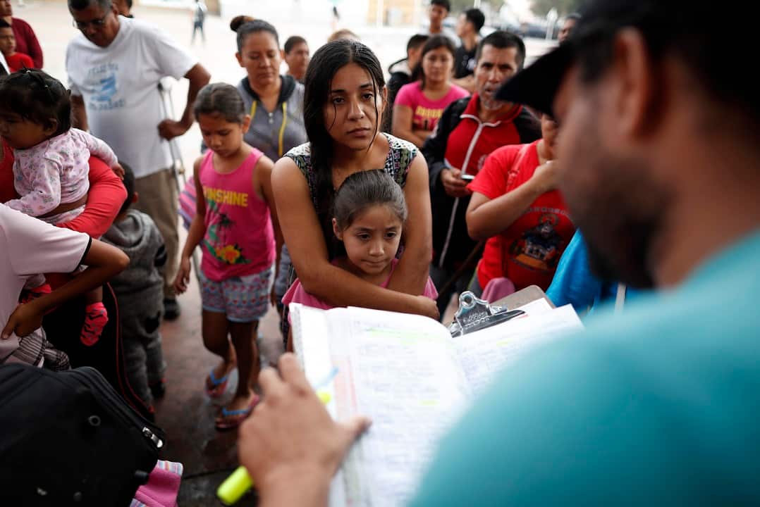 A woman from the Mexican state of Michoacan who did not give her name stands with her daughter as names are read off a list of people who will cross into the United States to begin the process of applying for asylum.