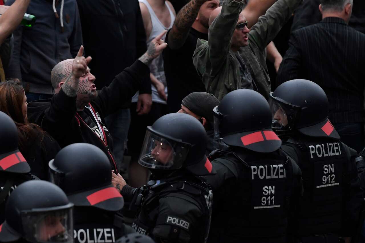 Right wing protesters gesture towards police in riot gear as they gather at the place where a man was stabbed in the night of the 25 August 2018, in East German city Chemnitz