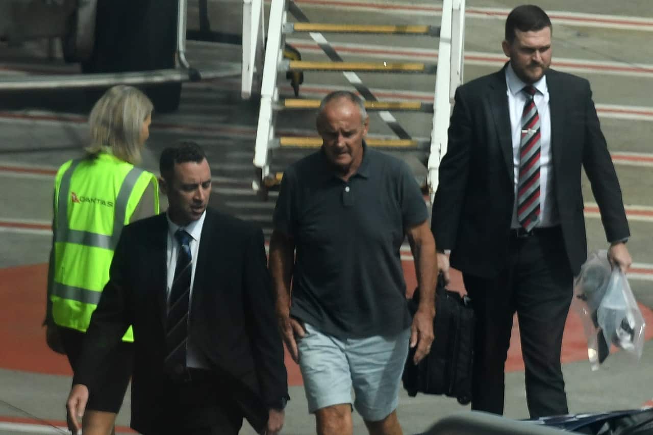 Chris Dawson (centre) is escorted by NSW Police detectives off a Qantas flight.