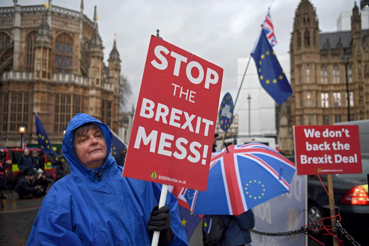 Brexit protesters shelter from a rain shower while Prime Minister Theresa May faces a no confidence vote in parliament.