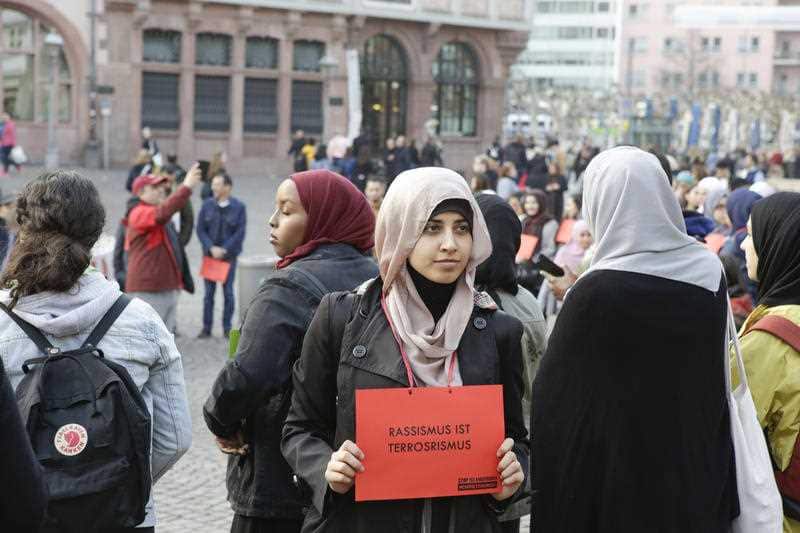 A woman carries a sign that reads "Racism is terrorism" at a vigil for Christchurch in Frankfurt, Germany.