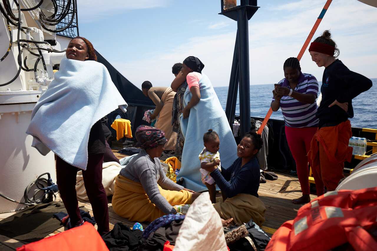 Migrants stand on the dock of the Sea-Watch rescue ship