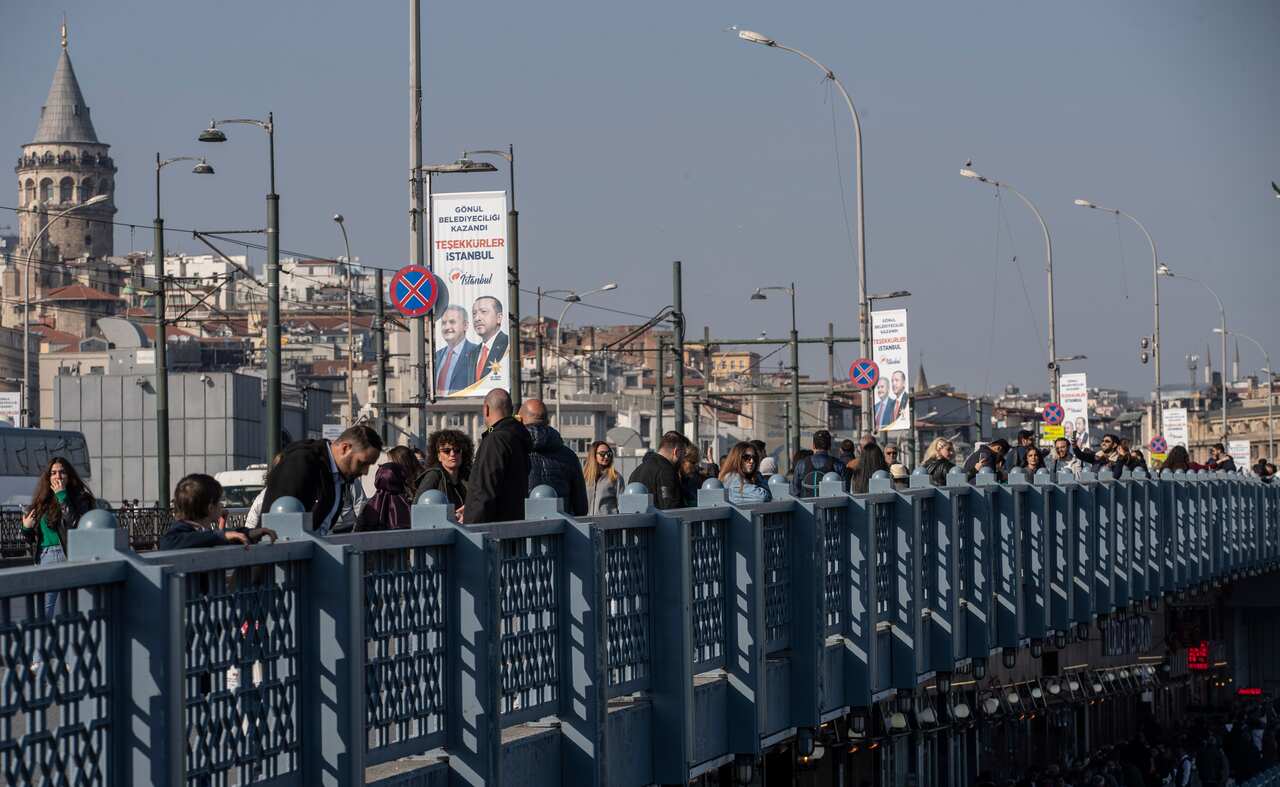 People walk on Galata Bridge as they pass in front of a picture of Turkish President Recep Tayyip Erdogan, in Istanbul, Turkey.