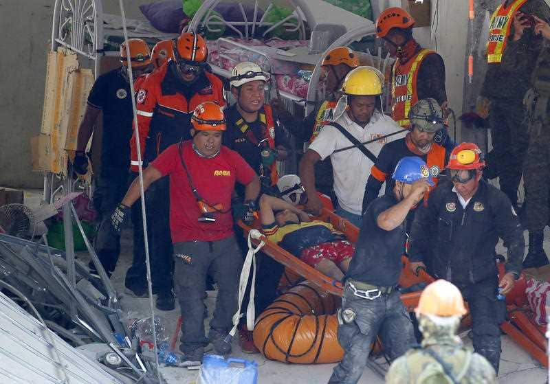 Rescuers carry a survivor that was pulled out from the rubble of a commercial building in the Porac township.
