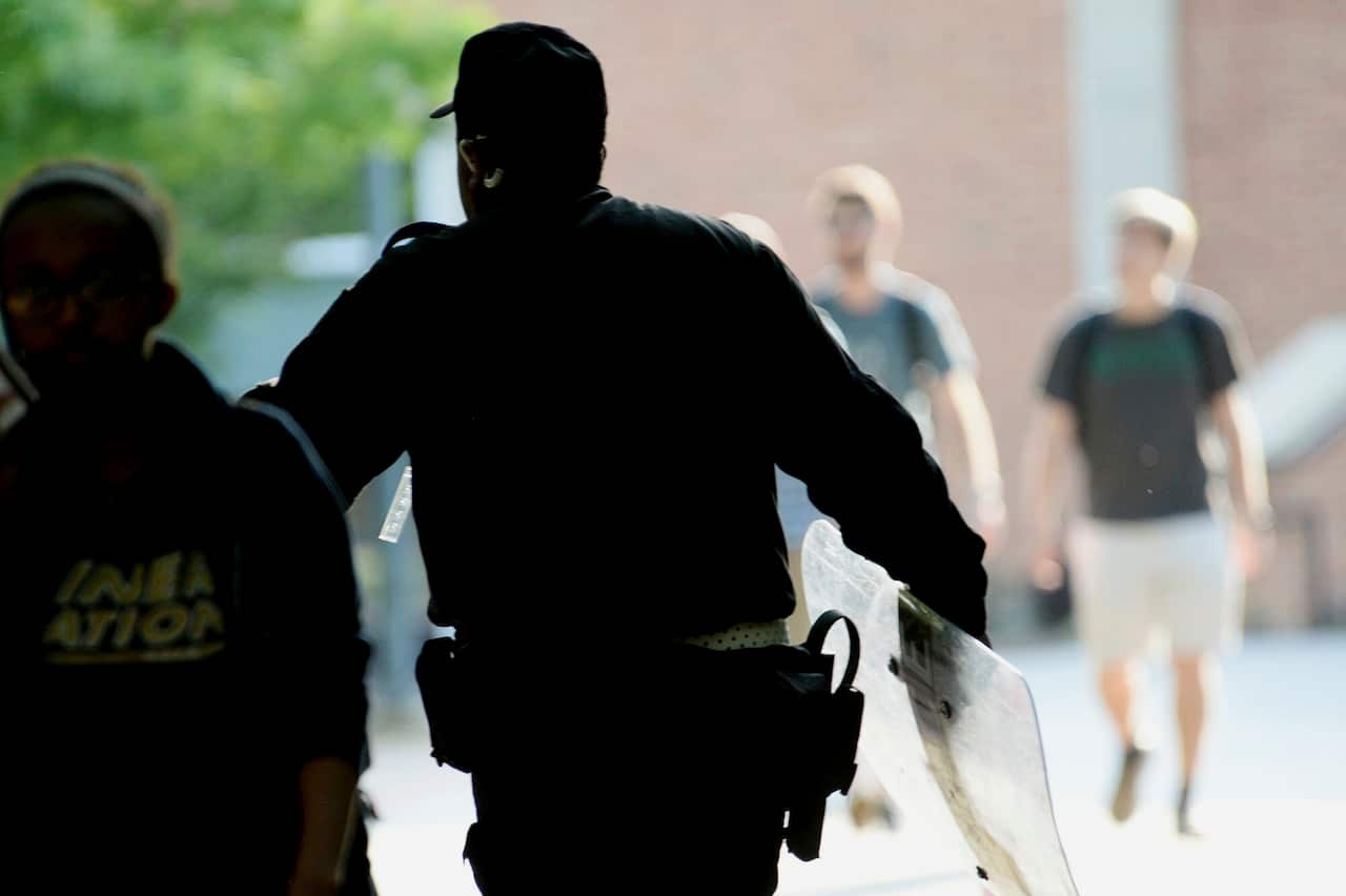 A UNC Charlotte campus police officer carries a tactical shield onto campus as students exit.