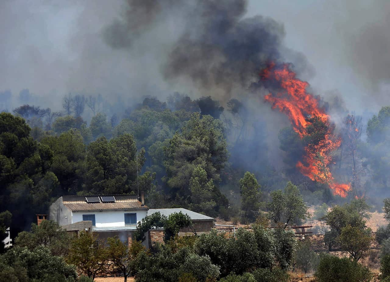 epa07677412 Fire and smoke rise near a house during a forest fire in La Torre de l'Espanyol in Tarragona, Spain, 27 June 2019. Fire emergency teams work to control the flames that have already burnt 4,00 hectares of land.  EPA/JAUME SELLART