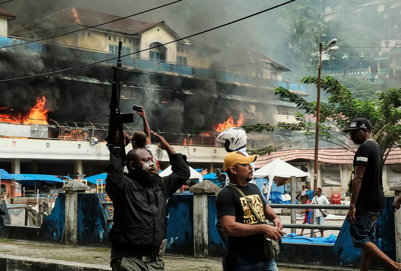 A Papuan police officer carries a riffle as he controls the crowd after protesters torched Buruni market during a violent protest in Fakfak.