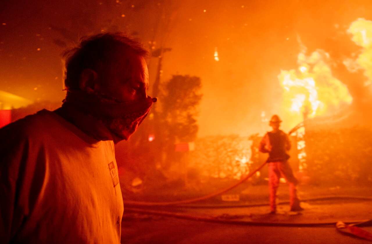 A man walks past a burning home during the Getty fire, Monday, Oct. 28, 2019, in Los Angeles, Calif. (AP Photo/ Christian Monterrosa)