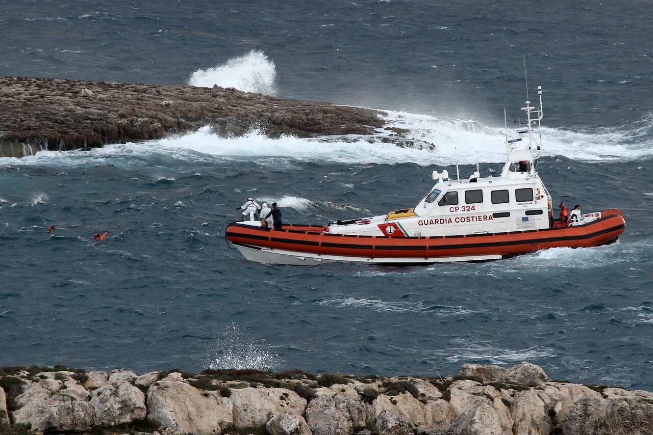 A rescuer in the water coordinates with a coast guard boat after retrieving a body at sea.