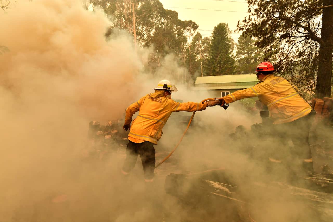 Firefighters hose down a burning woodpile during a bushfire in Werombi, 50 kilometres south-west of Sydney.