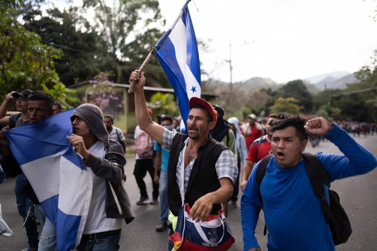 Migrants carrying Honduran flags walk along a highway in hopes of reaching the distant United States.