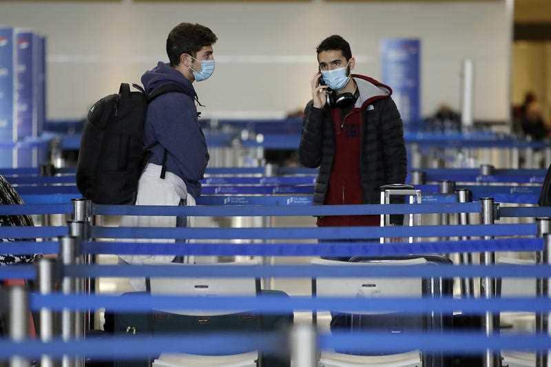 Travelers wearing masks wait to check-in luggage at the Los Angeles International Airport Sunday, March 15, 2020