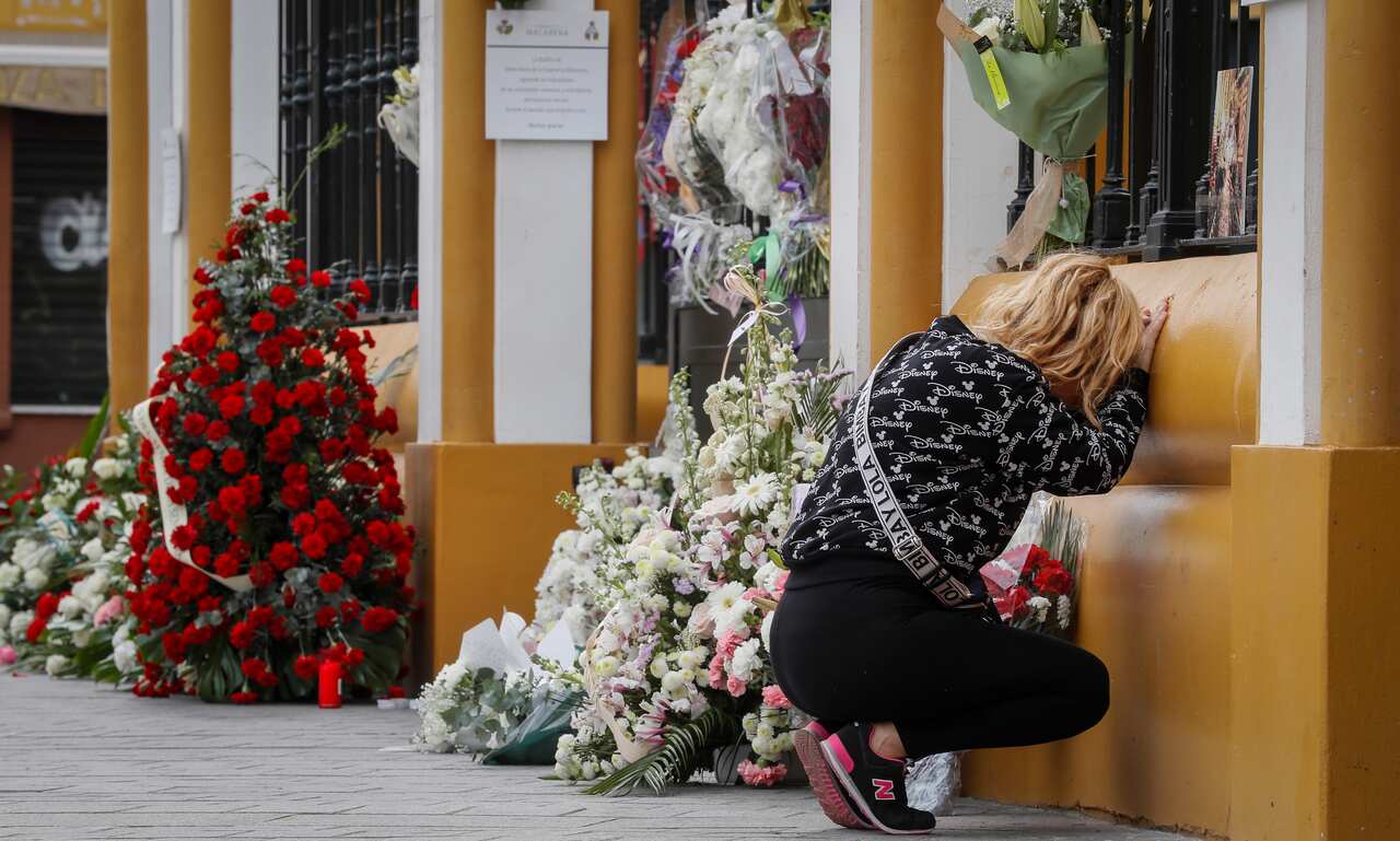 A woman prays next to some flowers laid in front of closed church in southern Spain.