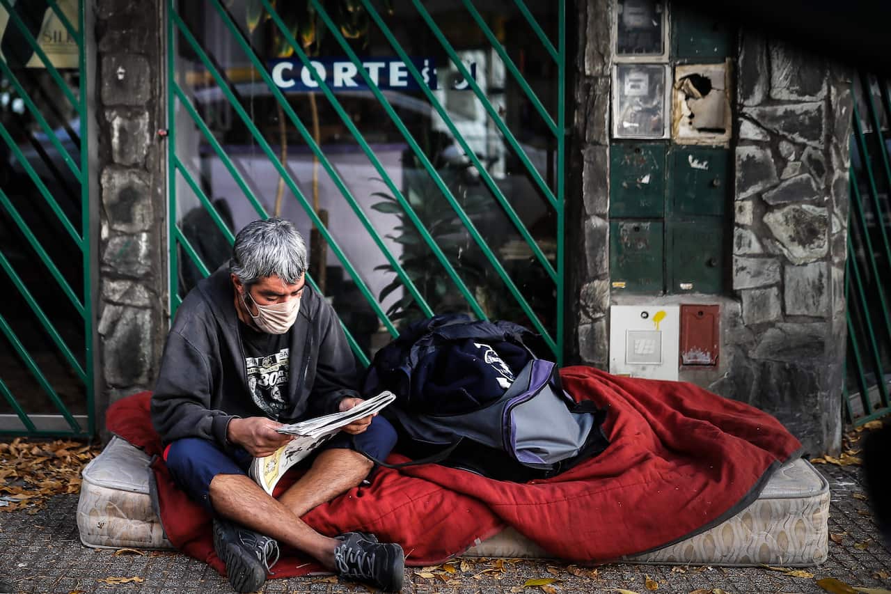 A homeless man sitting on a mattress reads newspaper, in Buenos Aires, Argentina.