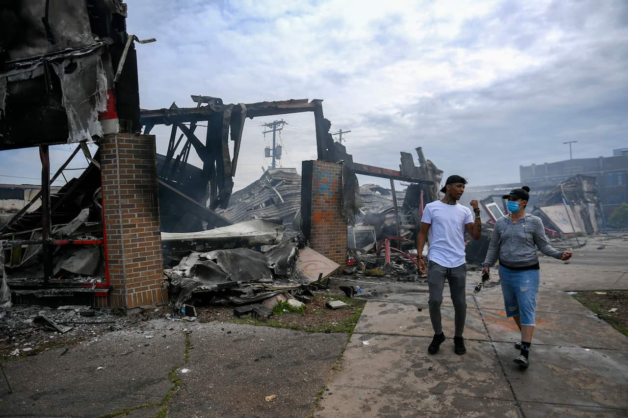 Pedestrians walk past destroyed buildings following riots over the death of George Floyd in the US.