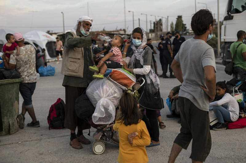 An Afghan man gives water to a child as refugees and migrants from the destroyed Moria camp wait to enter a new temporary camp, on the island of Lesbos.