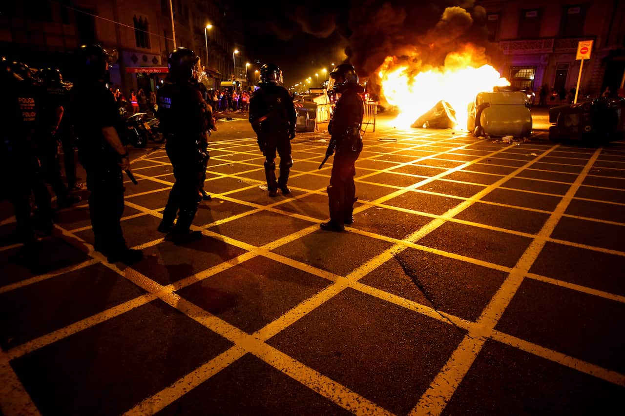 Riot police walk by trash containers on fire during the march.