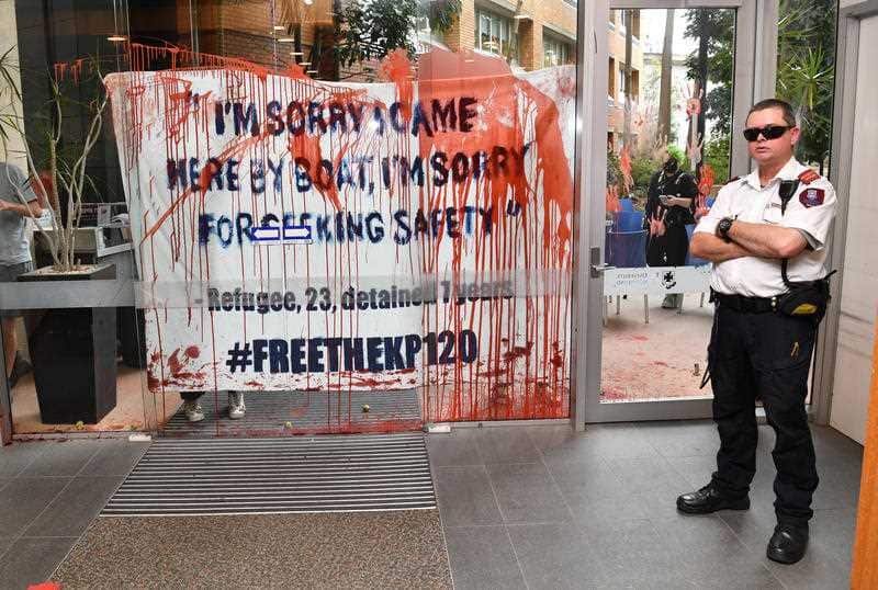 A security guard is seen guarding a door that has been smeared in fake blood