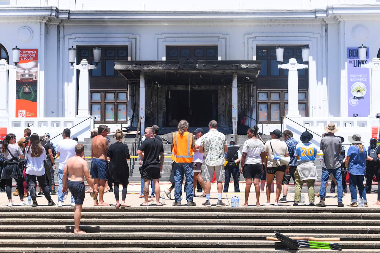 Protesters stand in front of the burned out entrance