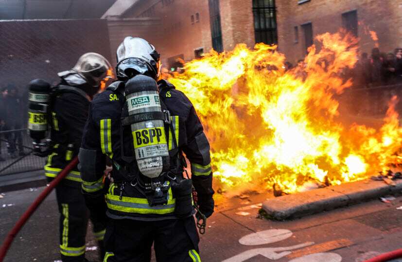 French firemen try to extinguish burning dustbins which obstruct the street, as students gather during a demonstration against police brutality.