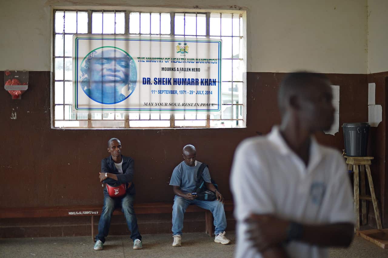 People sit beneath a banner mourning the death of doctor Sheik Umar Khan at Kenema government hospital, Sierra Leone, on August 16, 2014. 