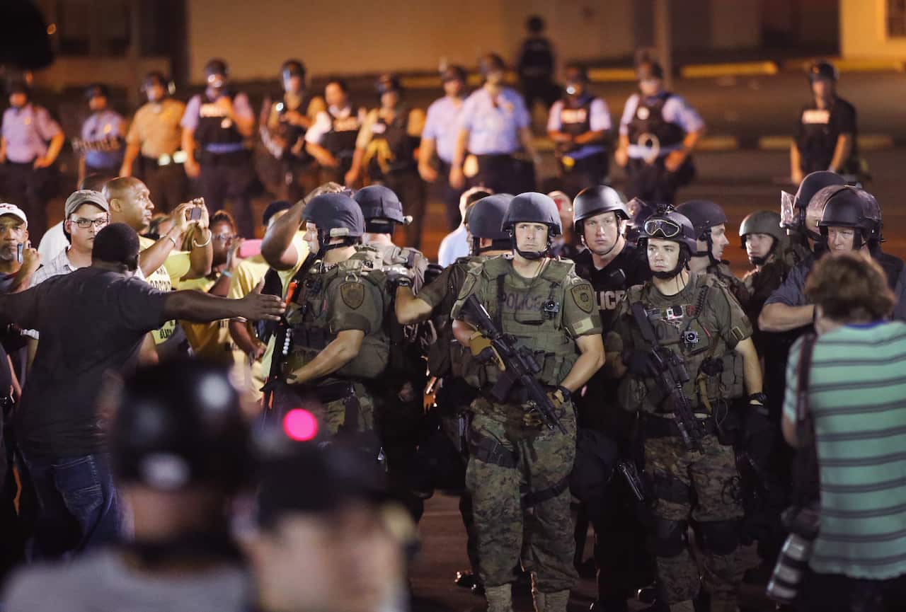 Police watch as demonstrators protest the killing of teenager Michael Brown on August 19, 2014 in Ferguson