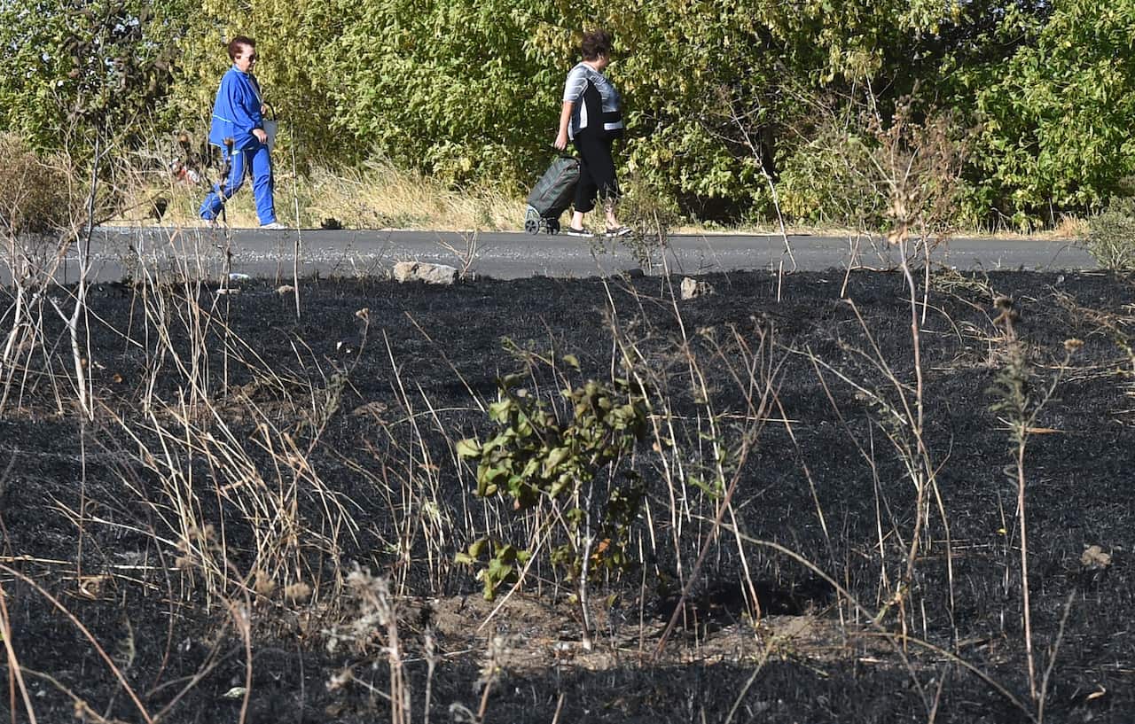 Women walk past burnt grass as they go back to their village on the outskirts of the southeastern port city of Mariupol.